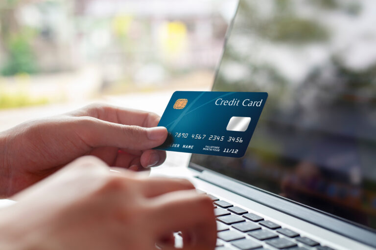 Woman hand holding blue credit card and using modern laptop, typing and texting. against defocus green nature outdoor. mobile payment ,online shopping concept
